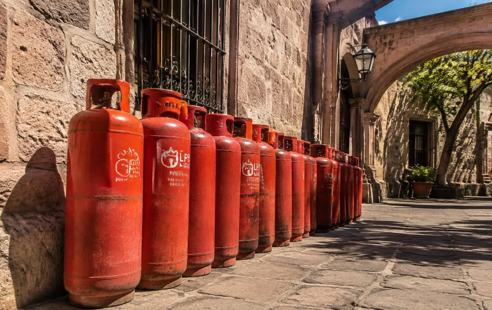 Cilindros de gas LP rojos alineados junto a un muro de cantera